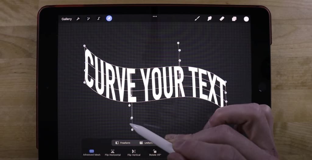 Photo of a hand holding a stylus and working with curved texts on Procreate